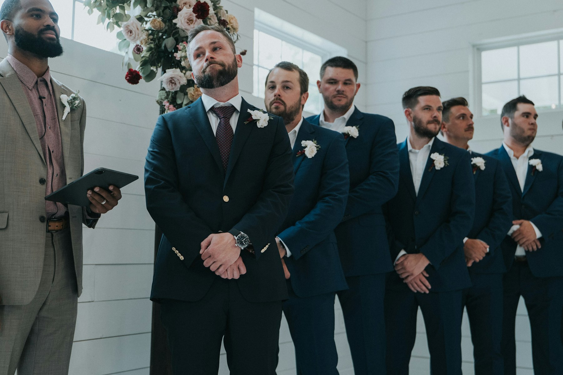 Groom watching the bride walk in, groomsmen behind him at a white barn wedding