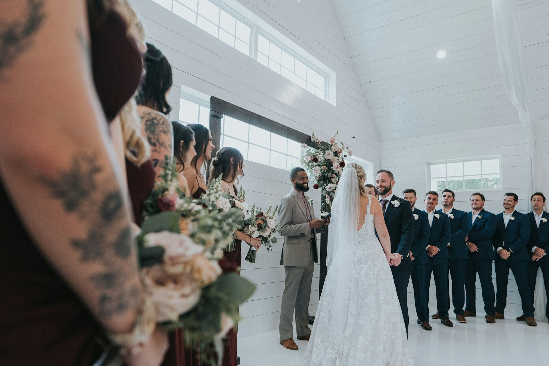 Ceremony seen from the bridesmaids' side, bouquet in front at a white barn wedding