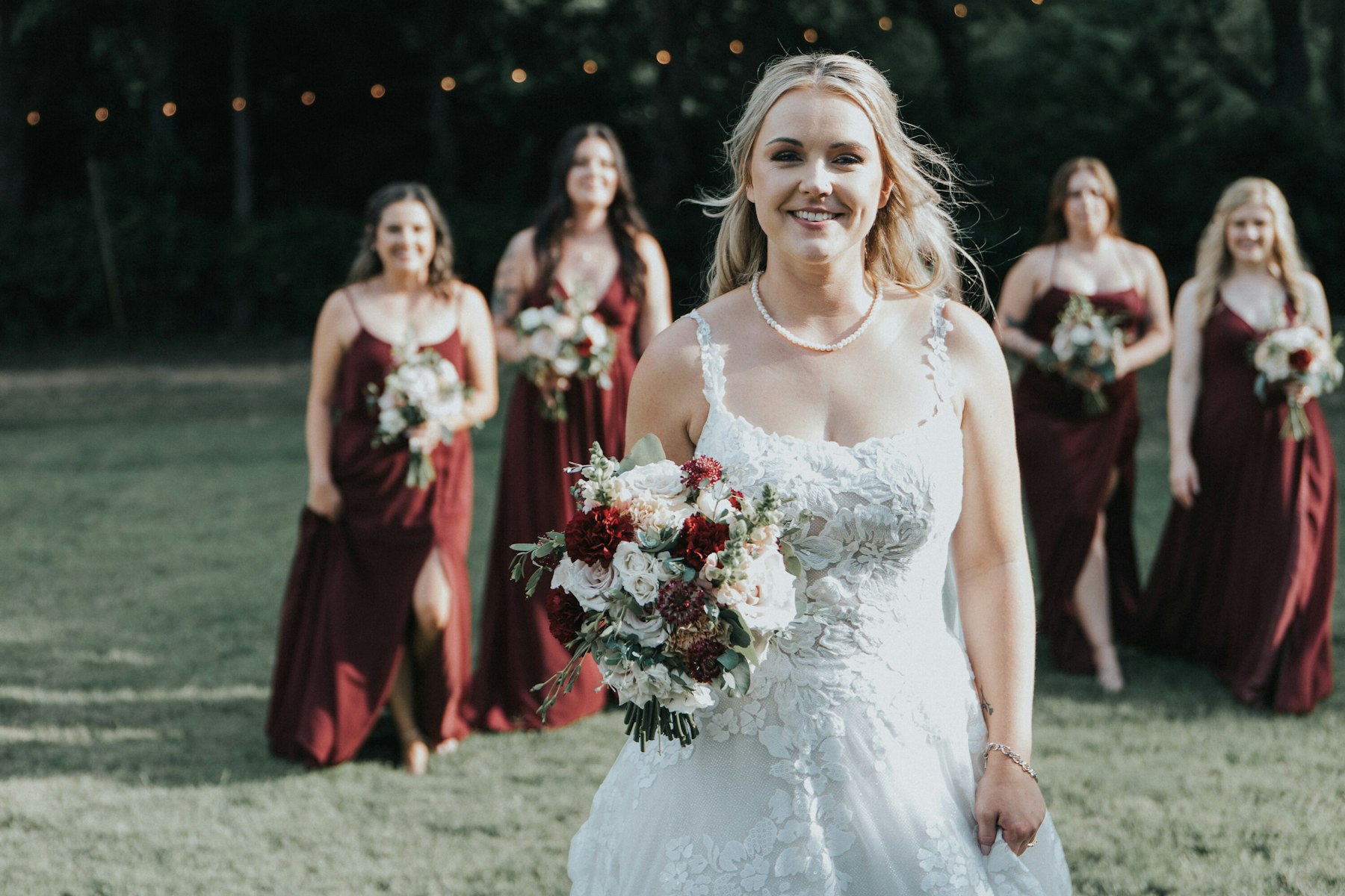 Bride with her bridesmaids in burgundy on the lawn at a white barn wedding