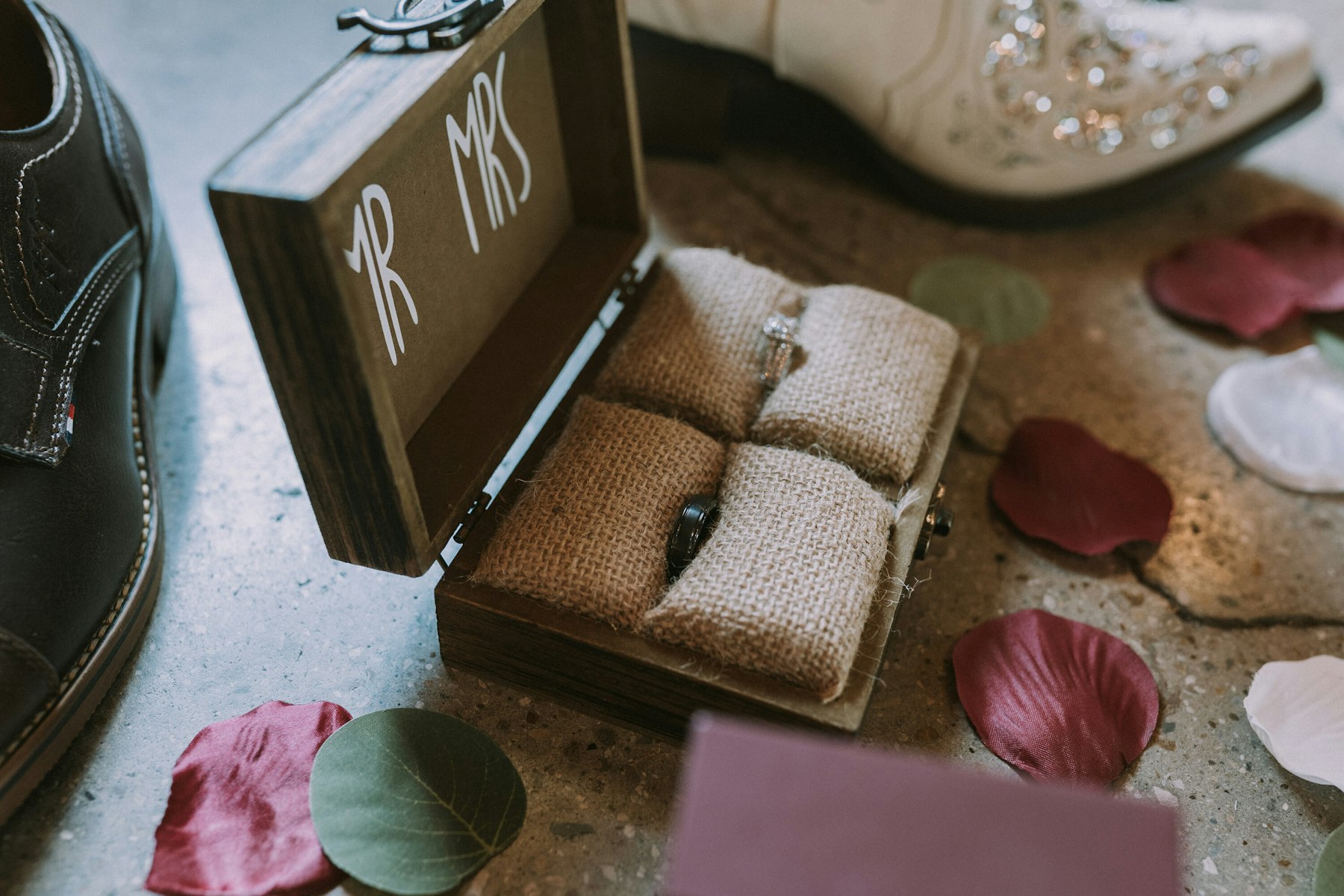 Wedding rings in a Mr and Mrs box beside the bride's boots at a rustic barn wedding