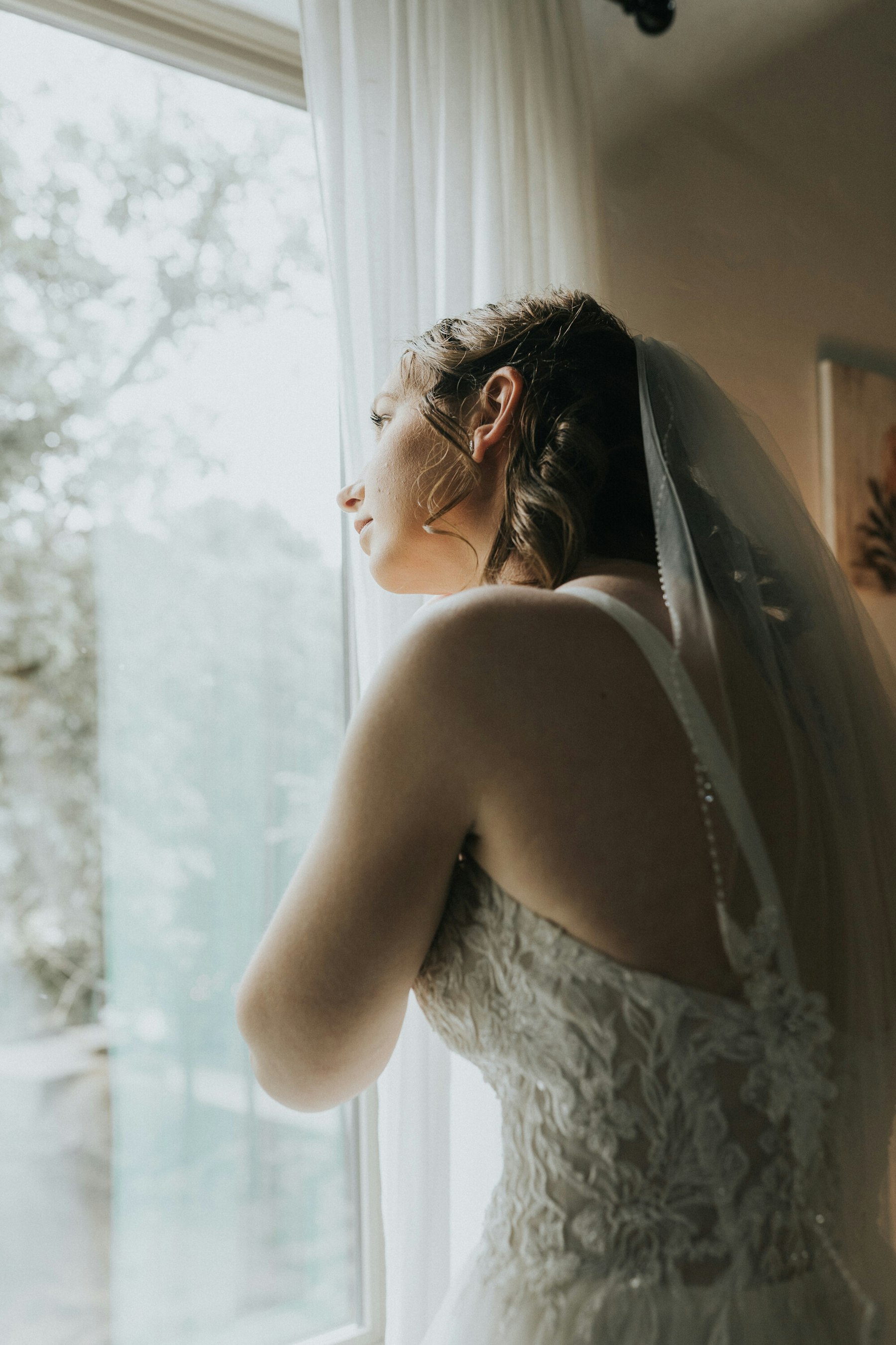 Bride gazing out the window in her veil at a rustic barn wedding