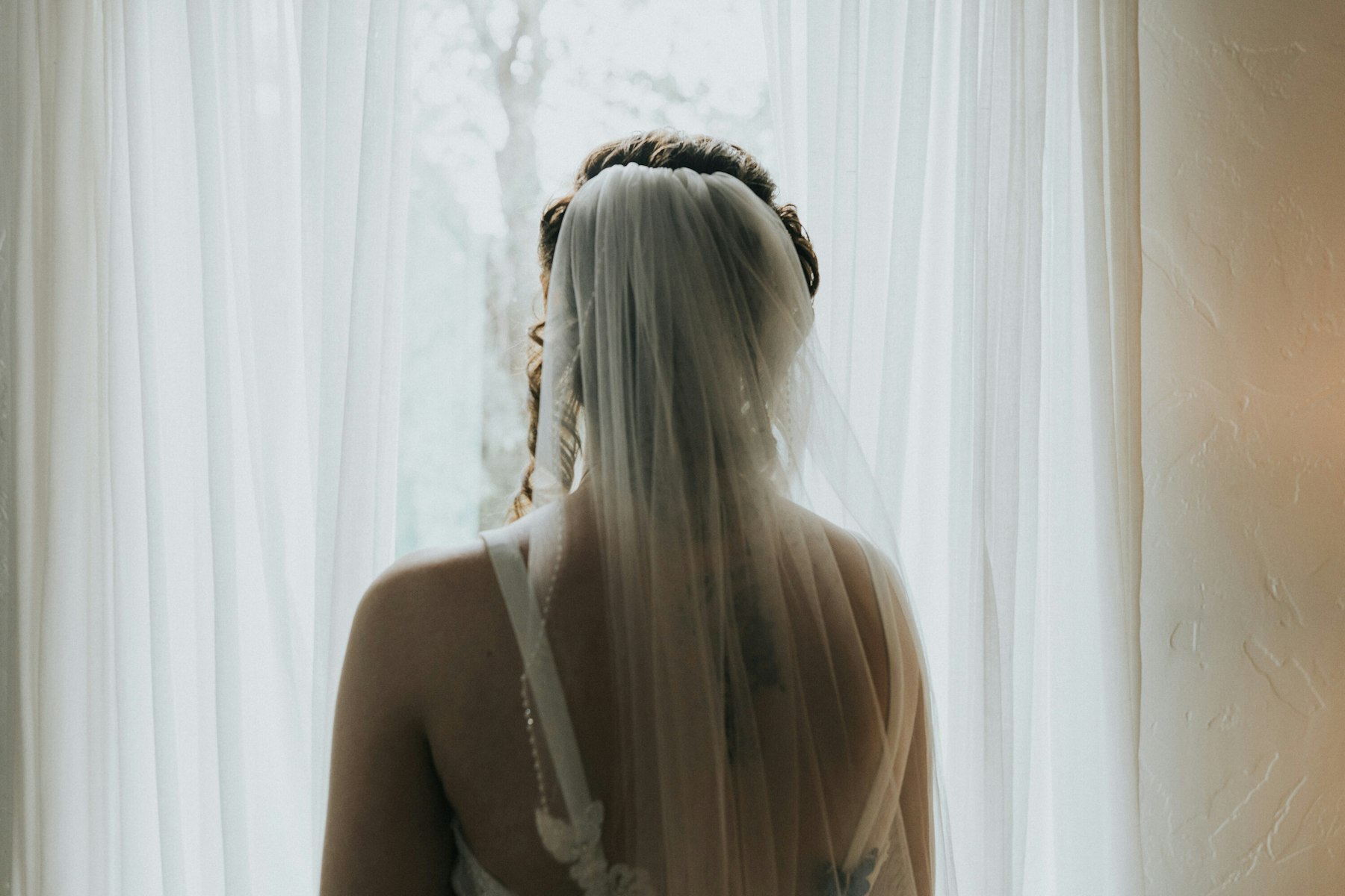 Bride's veil from behind at the window at a rustic barn wedding