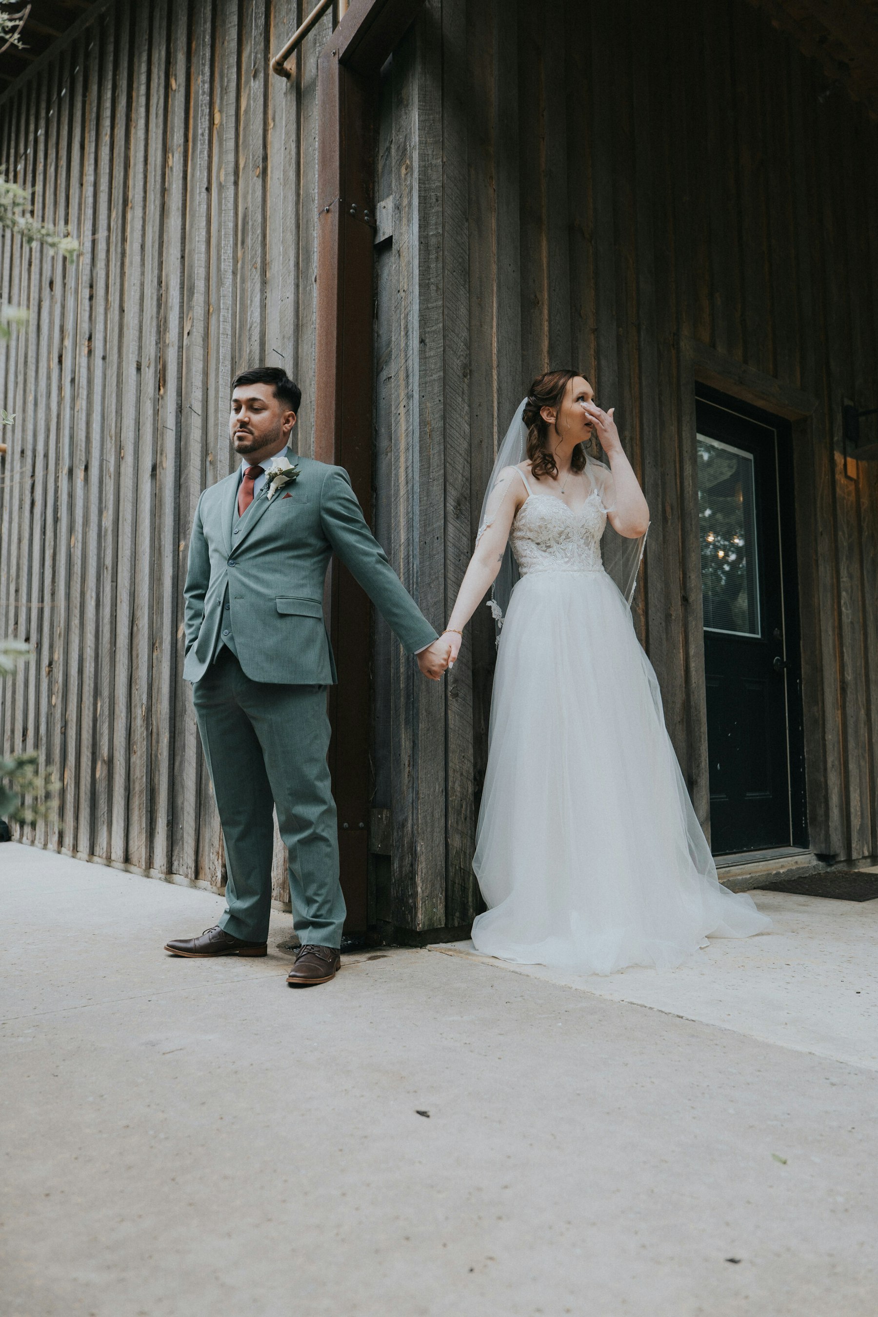 First touch: bride and groom holding hands around the corner of the barn at a rustic barn wedding