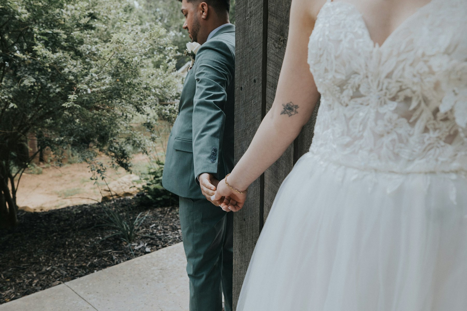 Bride and groom holding hands around the barn corner, close up at a rustic barn wedding