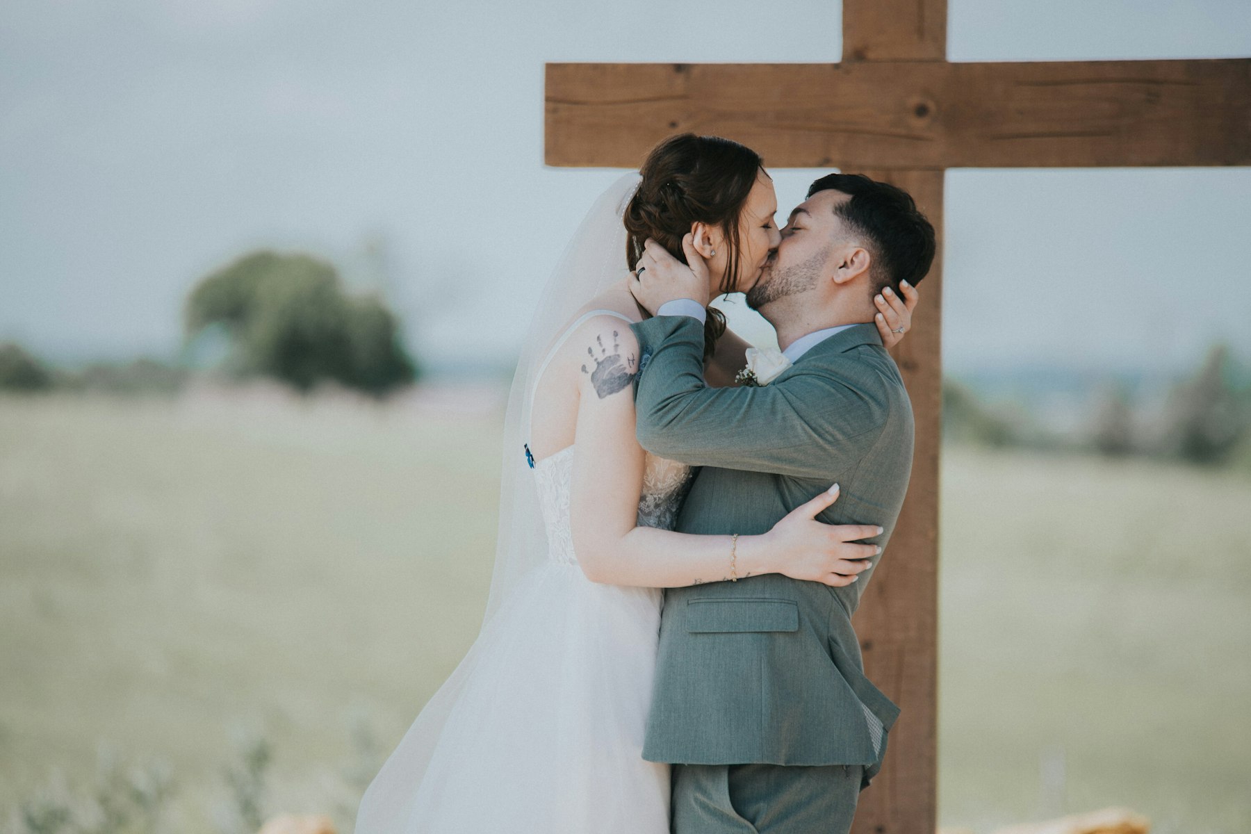 First kiss under the wooden cross at a rustic barn wedding