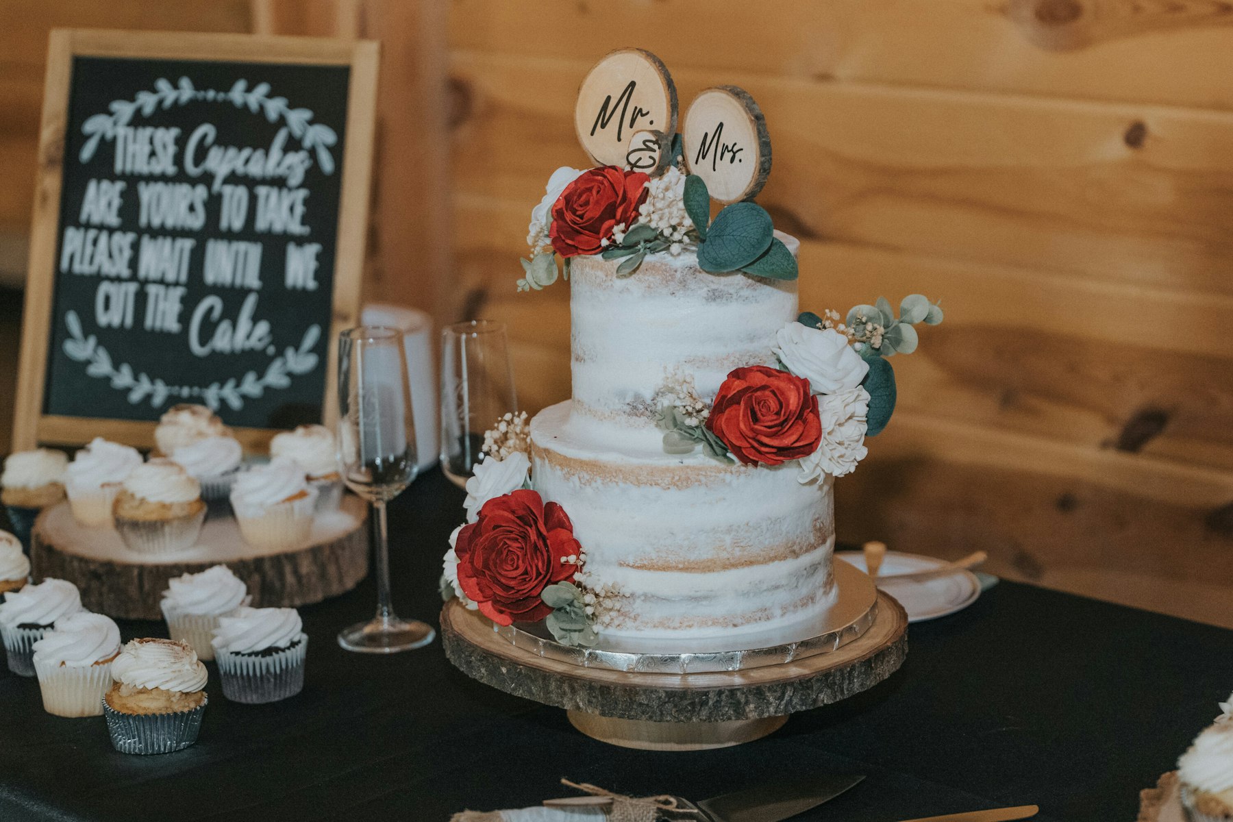 Naked wedding cake with red roses and cupcakes at a rustic barn wedding
