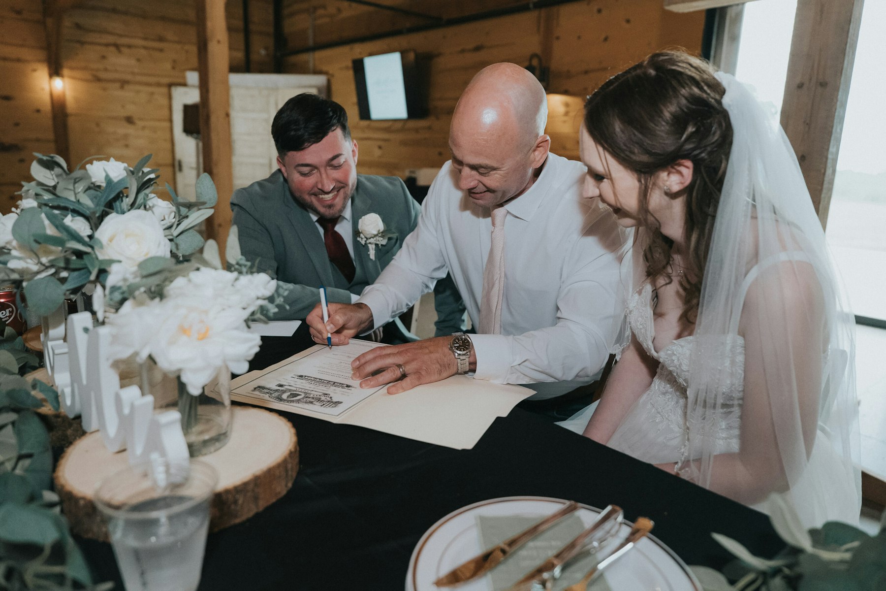 Bride and groom signing the marriage license at a rustic barn wedding