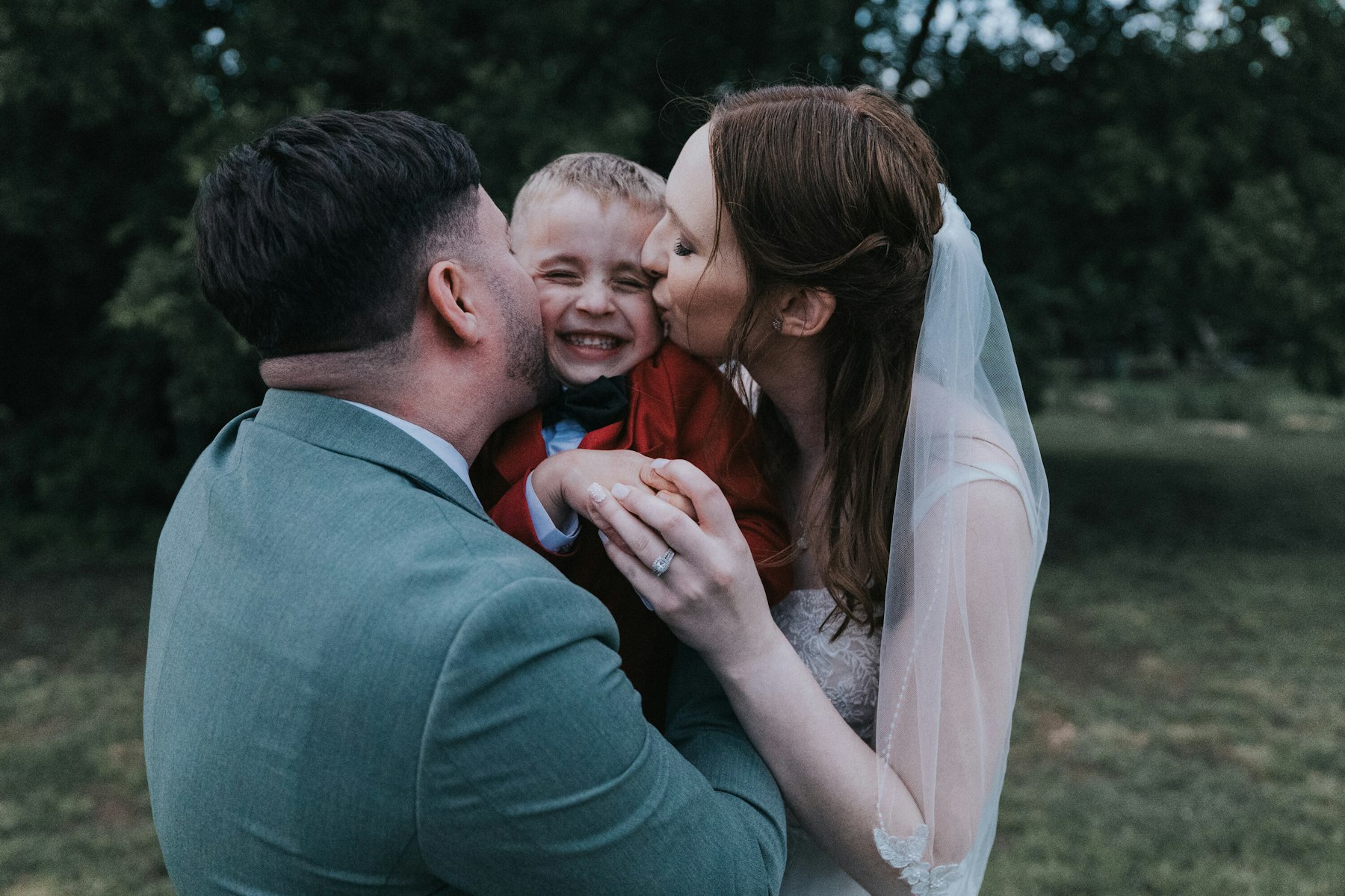 Bride and groom kissing their little boy at a rustic barn wedding
