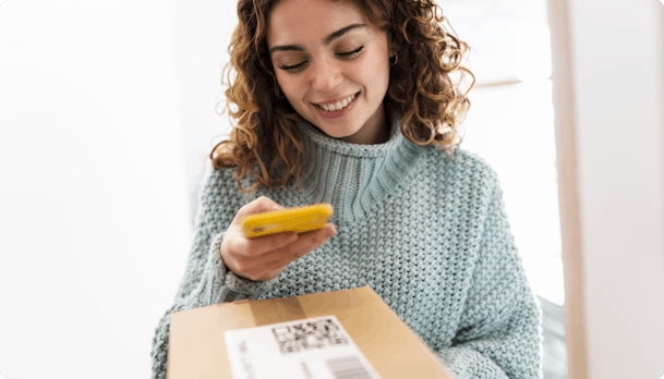 Smiling woman scanning QR code on parcel with phone
