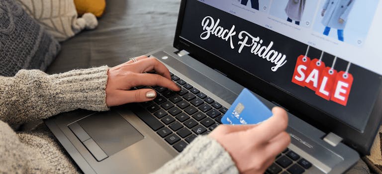 Close up of woman in grey jumper holding credit card in front of laptop screen which says Black Friday SALE