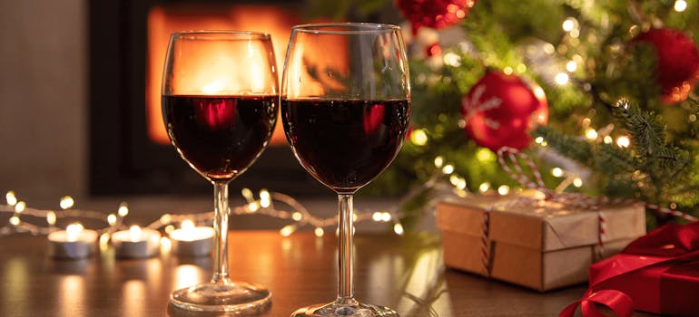 Two glasses of red wine and Christmas decorations on the table in front of a lit log burner