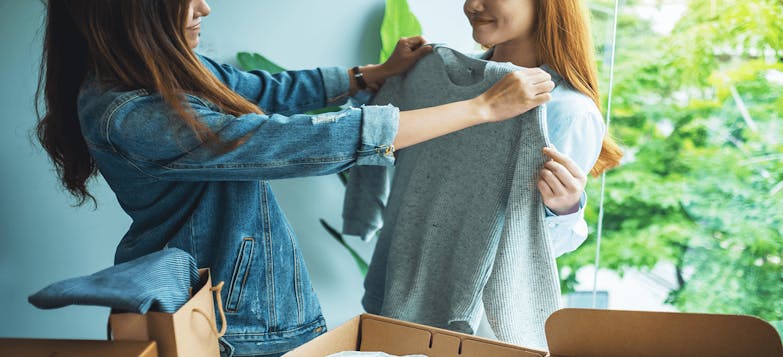 Two young women trying on clothes at home surrounded by packages