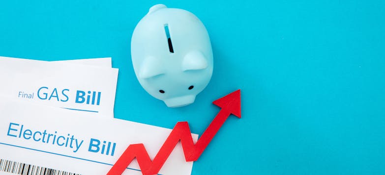 gas bill and electric bill against a blue background with a blue piggy bank and a red arrow pointing up