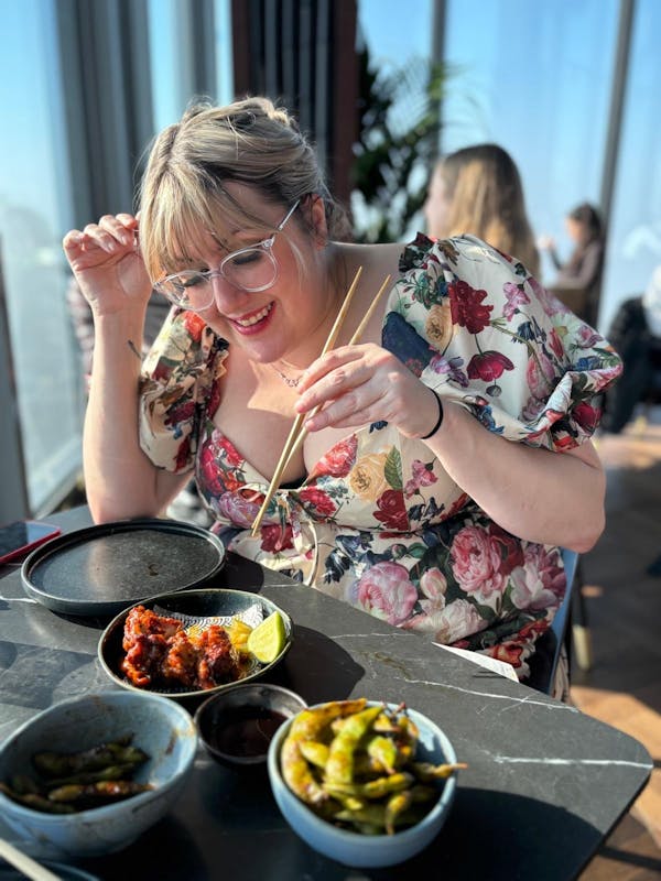 A girl on a sunny day moving chopsticks towards the Gordon Ramsay's famous Korean Fried Chicken at Lucky Cat Bishopsgate