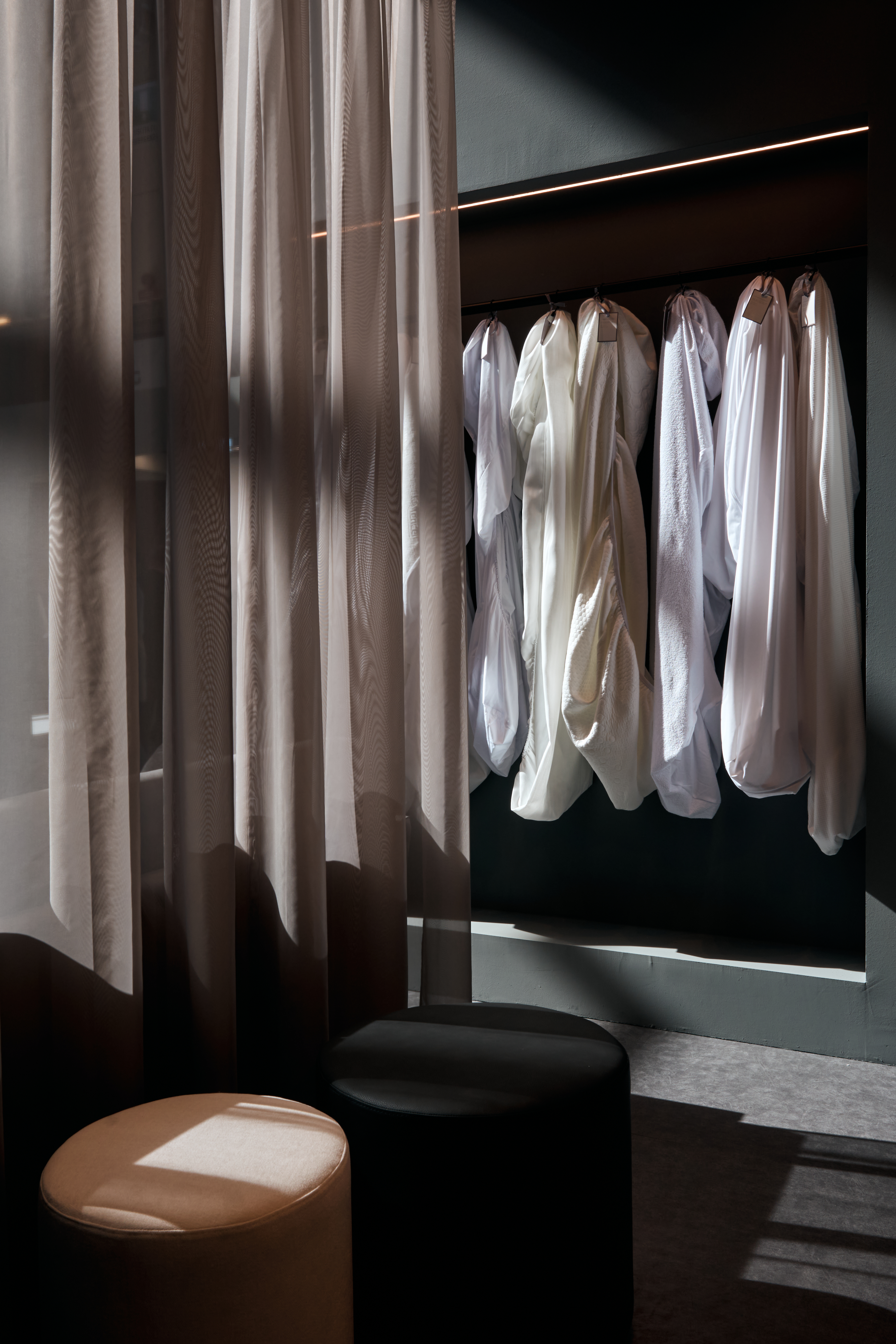 Showroom with sheer curtains, white garments on hangers and two poufs