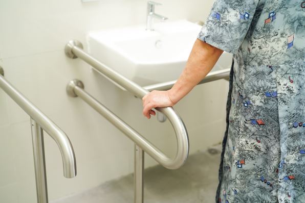 Літня жінка у ванній кімнаті для людей з обмеженими можливостями тримається за поручень