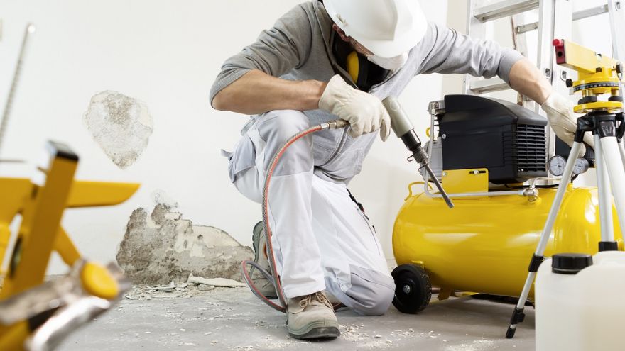 A man in work clothes and a protective mask working with a compressor