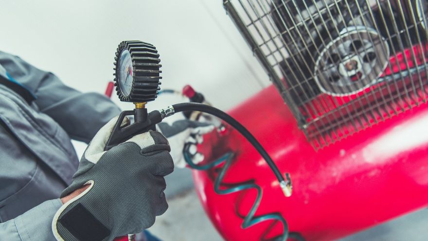 Ein Mann im Arbeitsanzug liest den Druckwert auf dem Manometer des Kompressors ab