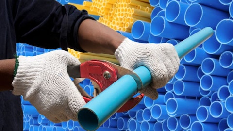 A construction worker cuts a plastic pipe against the background of blue and yellow pipes