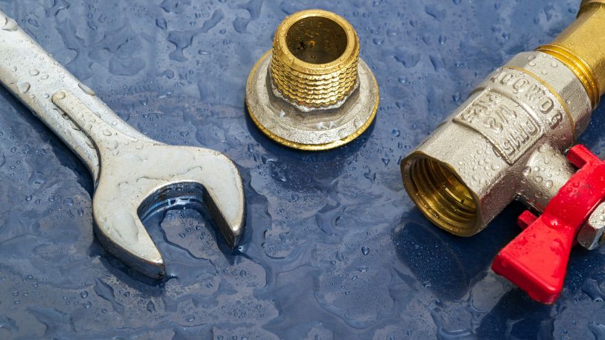 Płaski klucz hydrauliczny i mosiężny nypel z zaworem kulowym na mokrym niebieskim podłożu