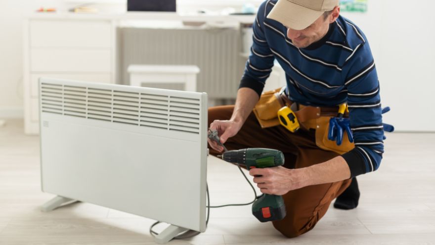 Instalator montuje grzejnik elektryczny w salonie z termostatem