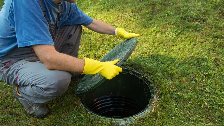 Szambonurek otwiera właz do szamba w ogrodzie