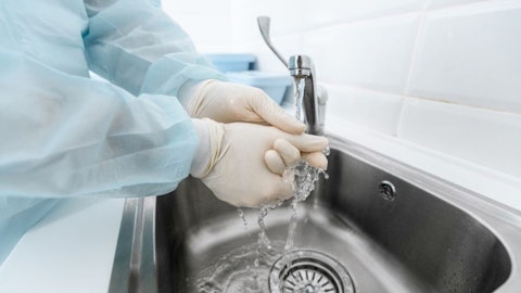 Lekarz myje ręce w kombinezonie ochronnym i rękawiczkach z zlewie z medyczną baterią lekarską