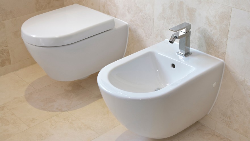 Chromowana bateria bidetowa natynkowa na bidecie obok miski WC w łazience