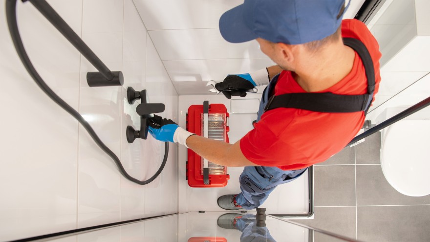 Instalator wymienia czarną słuchawkę prysznicową w łazience w kabinie