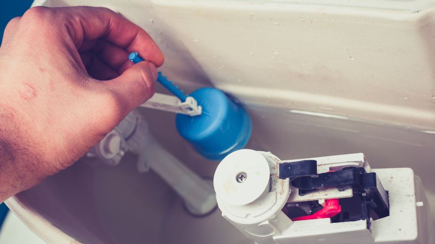 Instalator w łazience naprawia zepsuty zawór spłukujący z spłuczce od WC