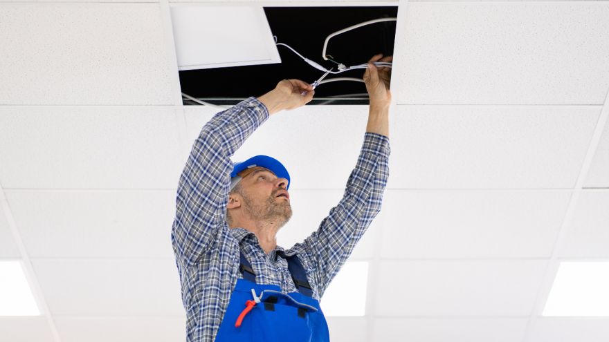 Instalator montuje panel LED na suficie w biurze