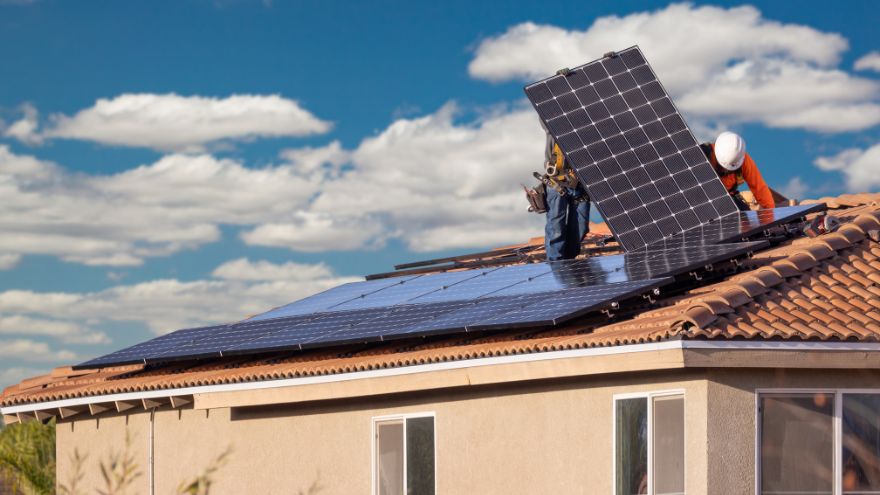 Instalatorzy montują panale fotowoltaiczne na dachu domu do instalacji solarnej na tle nieba