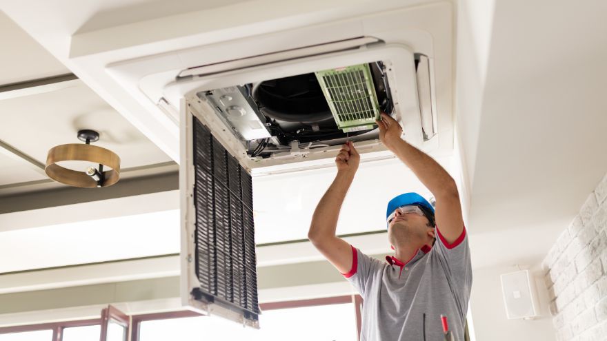 Instalator montuje klimatyzator sufitowy w salonie
