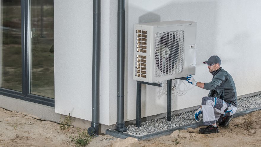 Instalator montuje pompę ciepła Monoblok na stelażu przed domem jednorodzinnym