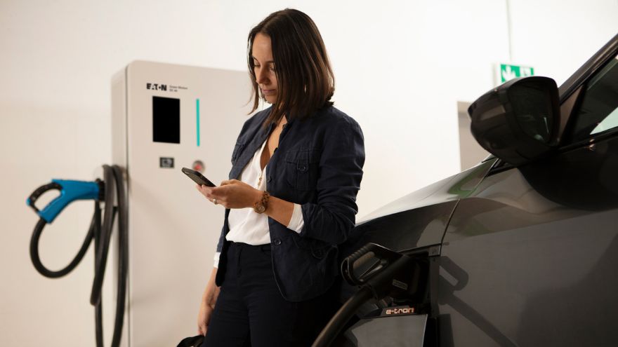 Kobieta przy ładowarce naściennej do samochodów wallbox ładuje pojazd elektryczny