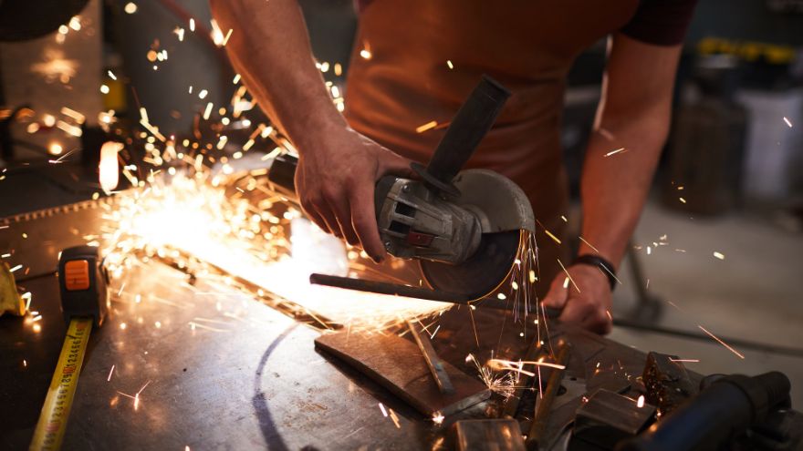 Pracownik fizyczny tnie metalowy pręt szlifierką z tarcza do cięcia w warsztacie