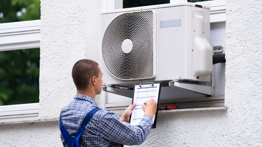 Instalator sprawdza stan techniczny jednostki zewnętrznej klimatyzacji przed budynkiem