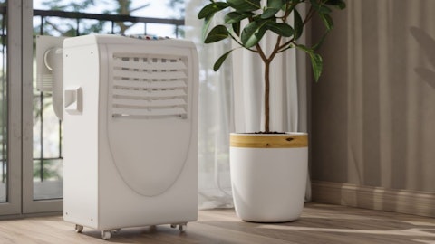 Klimatyzator przenośny na kółkach z rurą w salonie z rośliną przy balkonie