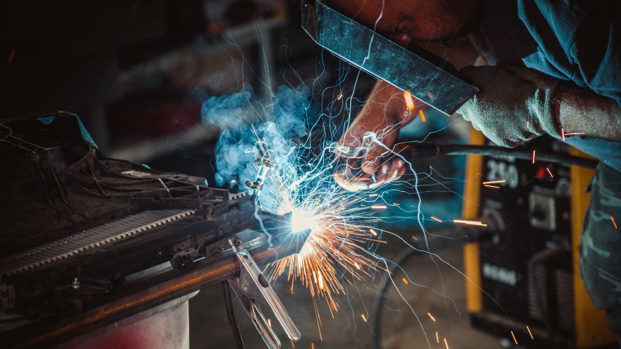Spawacz w przyłbicy spawalniczej łączy metalowe elementy w zakładzie