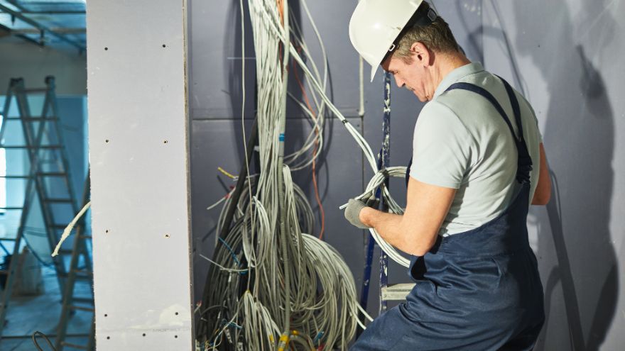 Technik elektryk podłącza przewody elektryczne do przewodów ochronnych PE. Zeruje napięcie w instalacji