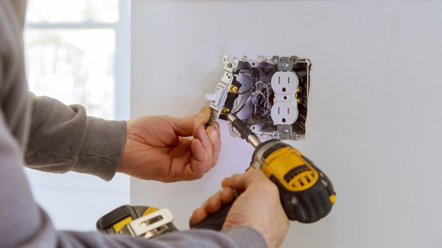 Instalator montuje osprzęt elektryczny, gniazdko elektryczne i włącznik światła w ścianie