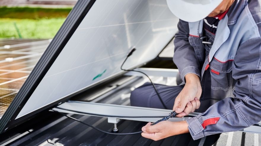 Instalator podłącza kabel solarny do instalacji fotowoltaicznej z panelami PV na dachu