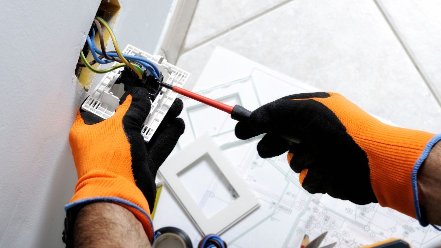 Instalator montuje włącznik elektryczny w rękawiczkach antyprzepięciowych o wysokiej klasie odporności elektrycznej