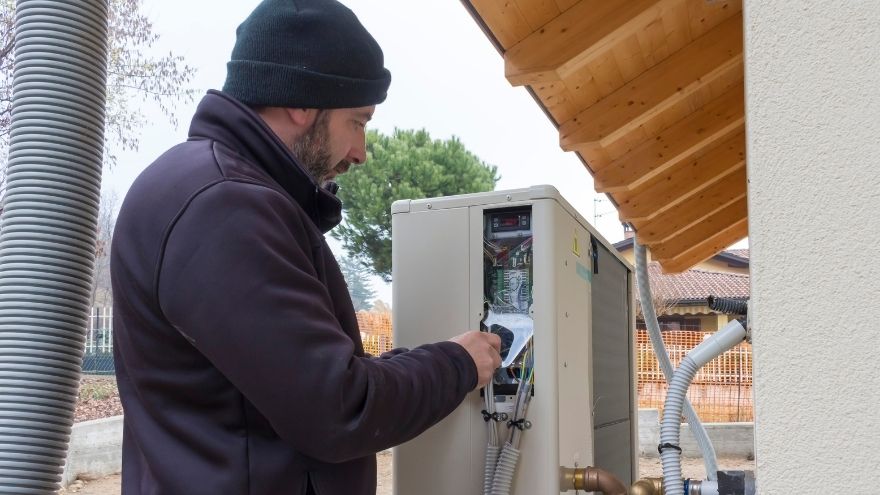 Instalator montuje powietrzną pompę ciepła przed domem jednorodzinnym