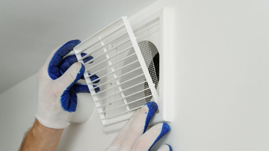 Instalator montuje kratkę wentylacyjną w mieszkaniu na ścianie
