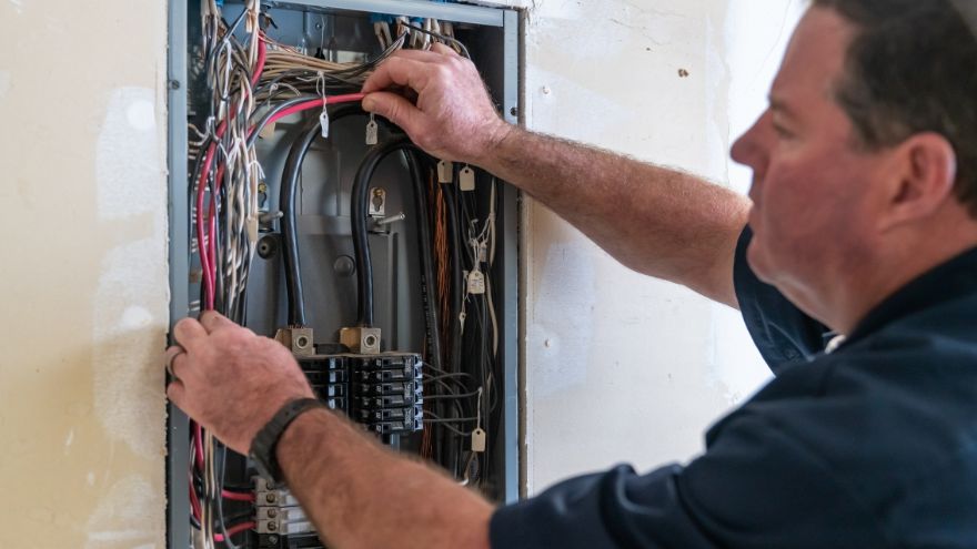 Instalator montuje kable elektryczne w rozdzielnicy podtynkowej w mieszkaniu