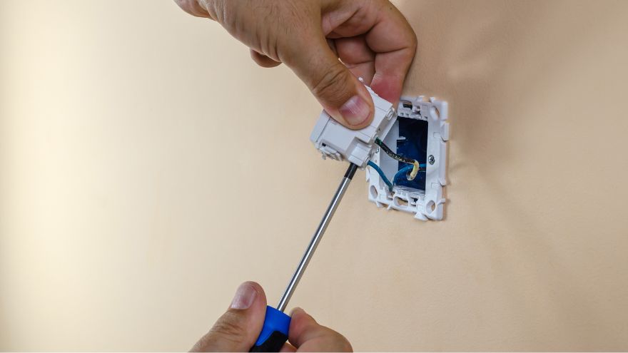 Elektroinstalator montuje gniazdko elektryczne w ścianie w automacie schodowym