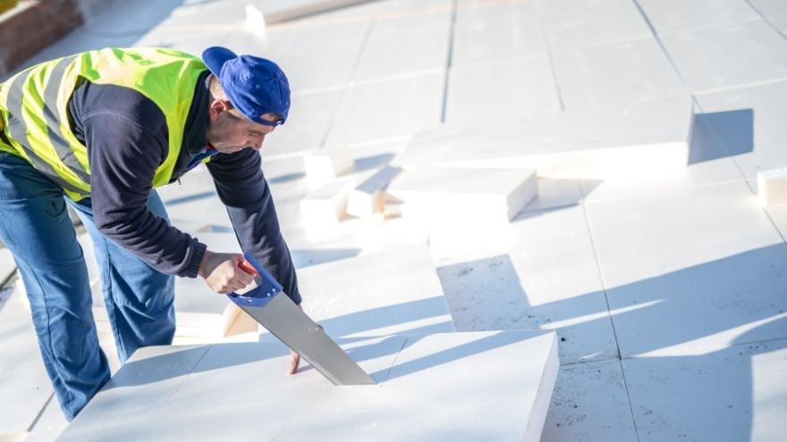 Instalator tnie styrodur piłą ręczną na dachu budynku do ocieplenia