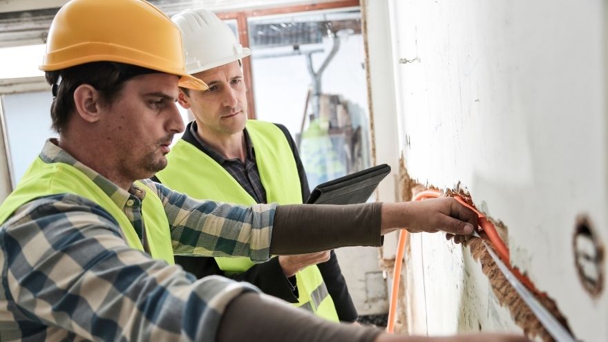 Kierownik budowy sprawdza postępy prac instalacyjnych prowadzenia kabla elektrycznego przez ścianę