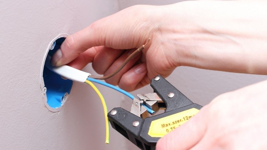Instalator przycina kable elektryczne w puszcze instalacyjnej w ścianie